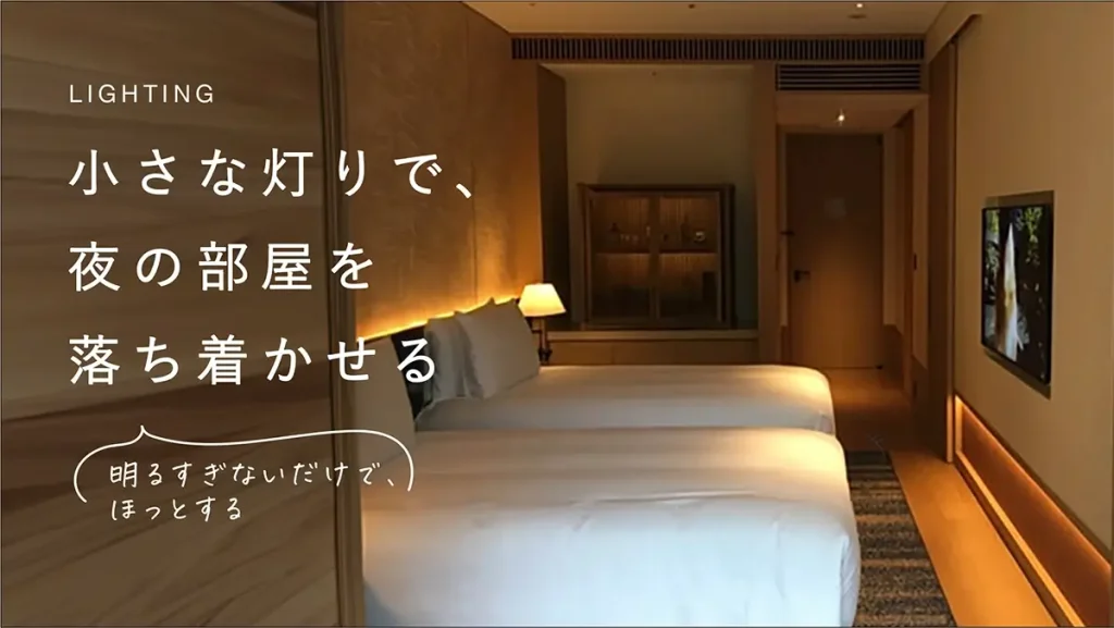 ベッドサイドと足元に小さな灯りが残るホテルの夜のベッドルーム