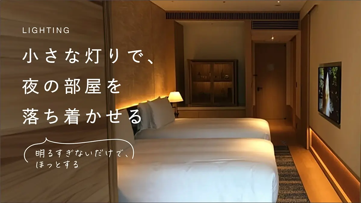 ベッドサイドと足元に小さな灯りが残るホテルの夜のベッドルーム